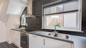 Eine moderne Küche mit Fenster, Edelstahlgeräten und einer schwarzen, gefliesten Rückwand.