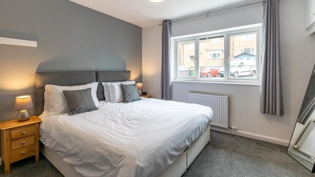 Ein Schlafzimmer mit Bett, Nachttischen, einem Fenster mit Vorhängen und einem Heizkörper.