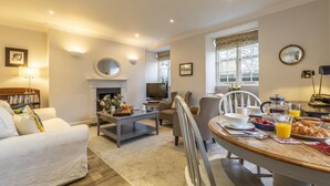A living room with a fireplace, a television, and a dining area with breakfast items. - 2 Bed in Bath (oc-bhr14) (Bath)