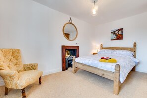 Ein Schlafzimmer mit einem hölzernen Bett, einem Sessel, einem Spiegel und einem Kamin.