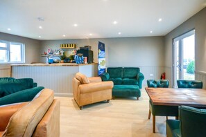 A hotel lobby with a bar area, green sofas, a wooden table, and a large window.