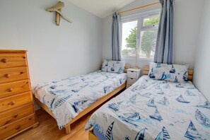 A bedroom with two single beds, a wooden dresser, a nightstand, and a window with curtains. - 2 Bed in Padstow (oc-p00551) (Penrose)