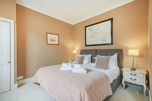 Hotellihuone, jossa on sänky, yöpöydät, yölamppu, kehystetty taideteos ja ovi.