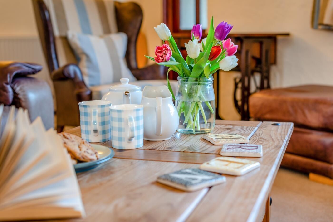 Een houten tafel met een bloevas vol tulpen, een theepot, kopjes en een boek.