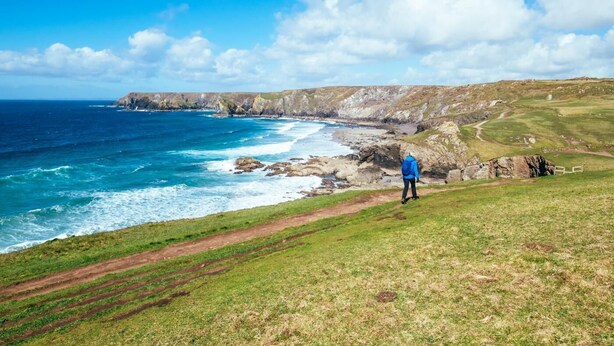 A coastal landscape with a person standing on a grassy hill overlooking the sea and cliffs. - 1 Bed in Padstow (oc-p00554) (Saint Merryn)