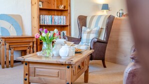 A cozy living room with a wooden coffee table, a bookshelf, a comfortable armchair, and a lamp. - 1 Bed in Padstow (oc-p00554) (Saint Merryn)