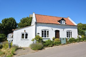 A white building with a red-tiled roof, a sign reading 'HAPPISBURGH,' and a green gate. - 2 Bed in Happisburgh (oc-1634) (Happisburgh)