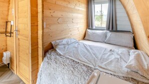Quarto aconchegante com teto inclinado de madeira, cama com roupa de cama cinza e janela com cortinas.