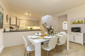 A modern kitchen with white cabinets, a dining area with white chairs, and a staircase leading to another level. - 2 Bed in Bath (oc-bhr19) (Bath)