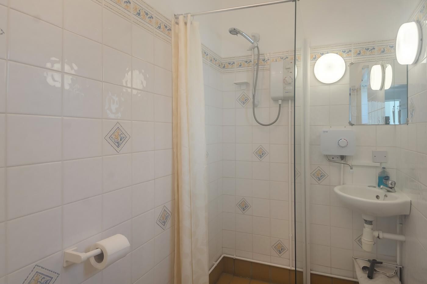 A bathroom with a glass shower enclosure, a toilet paper holder, a sink with a mirror, and a wall-mounted heater.