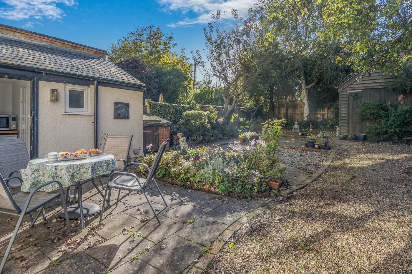 A garden with a table and chairs, surrounded by various plants and a small shed.