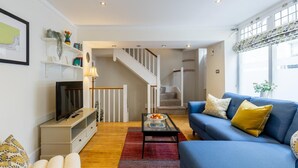 A modern living room with a blue sofa, a flat-screen TV, and a staircase leading to an upper floor. - 2 Bed in Bath (oc-bhr24) (Bath)