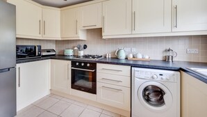 A modern kitchen with white cabinets, a built-in oven, a washing machine, and a countertop with various appliances. - 3 Bed in Wangford (oc-75sare) (Wangford)