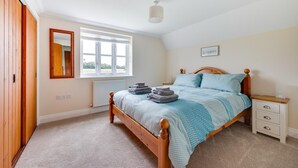 A bedroom with a wooden bed, a nightstand, a bedside table, a window with white curtains, and a mirror on the wall. - 3 Bed in Wangford (oc-75sare) (Wangford)