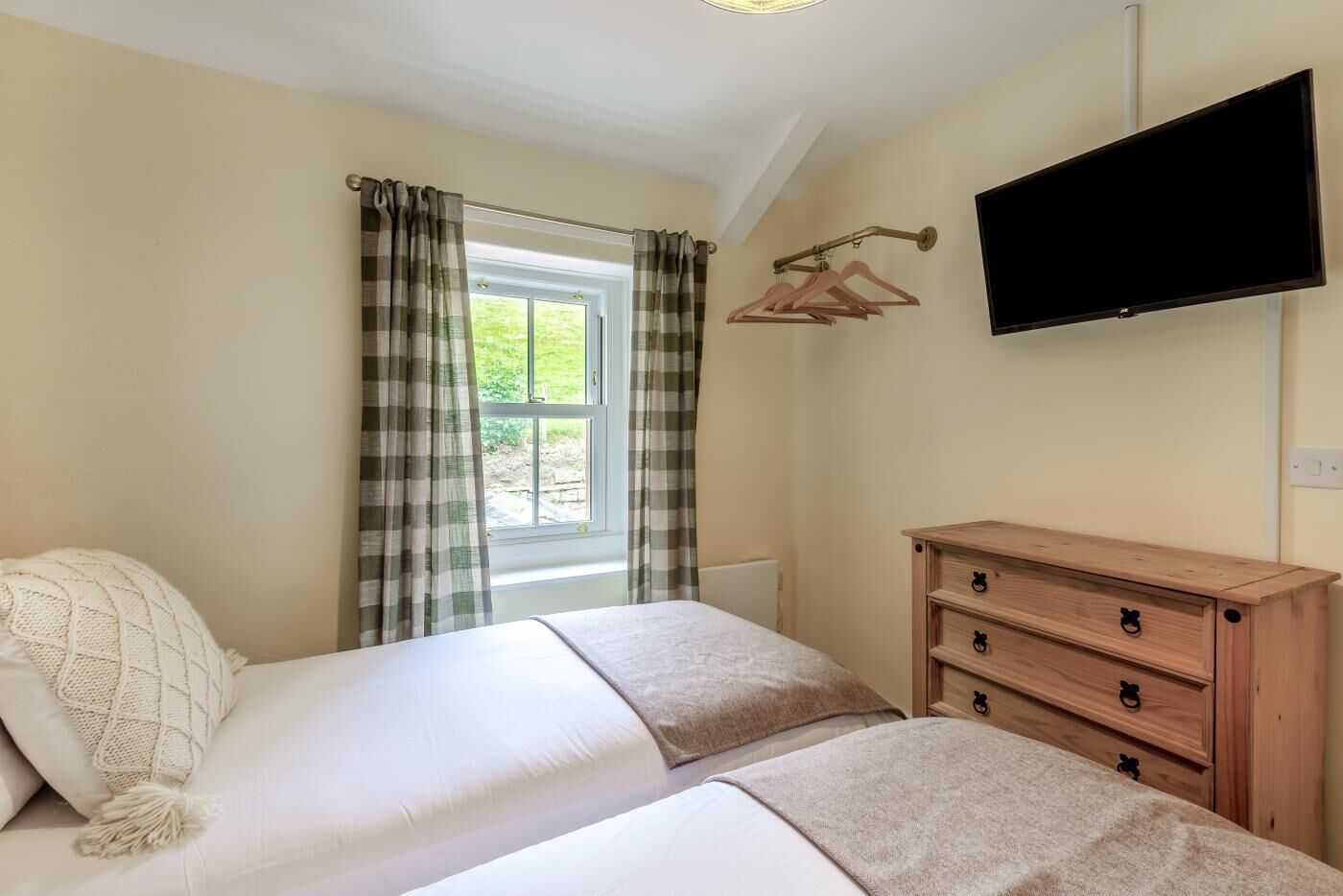 Une chambre avec deux lits, une commode en bois, une télévision et une fenêtre avec des rideaux.