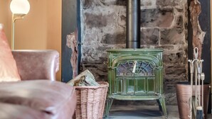 A rustic room with a stone wall, a green stove, a wicker basket, and a metal bucket labeled "KINDL". - 2 Bed in Staffield (oc-j32453) (Staffield)