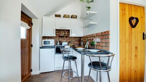 A compact kitchen with white cabinets, a brick backsplash, a microwave, a toaster, and two bar stools. - 1 Bed in Acle (oc-1256) (Limpenhoe)