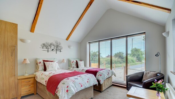 A bedroom with two beds, a wooden wardrobe, a desk, a chair, and large windows with blinds. - 1 Bed in Acle (oc-1256) (Limpenhoe)