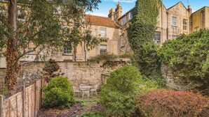 A stone courtyard with a table and chairs, surrounded by lush greenery and a stone wall. - 2 Bed in Bath (oc-bhr25) (Bath)