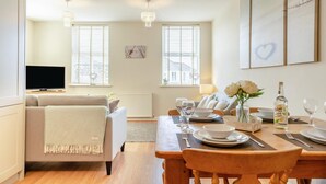 A modern living room with a sofa, dining table set for four, and a television in the background. - 2 Bed in Seahouses (oc-nb1944) (Seahouses)