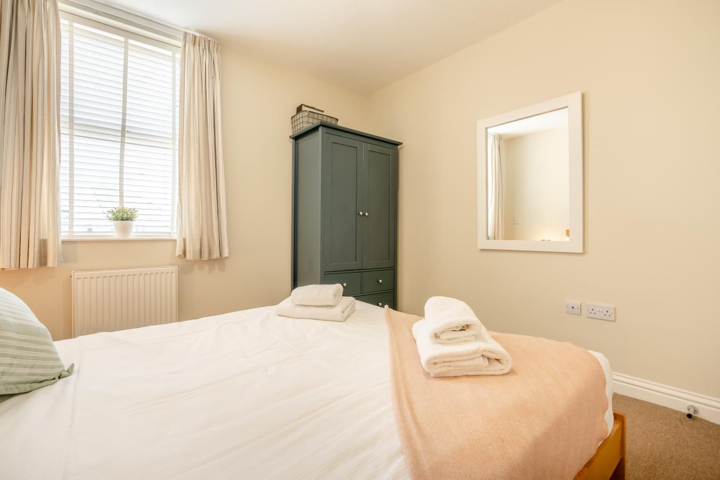A hotel room with a bed, a wardrobe, a window with curtains, and a mirror on the wall.