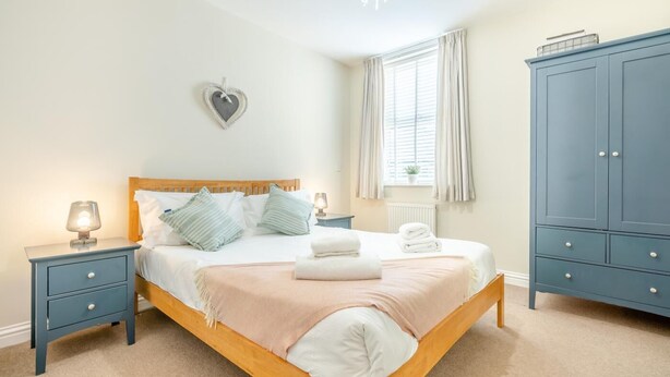 A bedroom with a wooden bed, bedside tables, a wardrobe, and a heart-shaped decoration on the wall. - 2 Bed in Seahouses (oc-nb1944) (Seahouses)