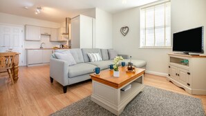 A modern living room with a grey sofa, wooden coffee table, and a television on a cabinet. - 2 Bed in Seahouses (oc-nb1944) (Seahouses)