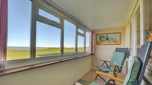 Ein Balkon mit drei Stühlen, einem Tisch mit einer Flasche und einem Gemälde an der Wand.