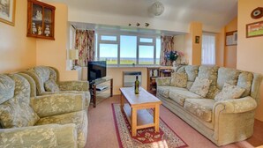 Ein Wohnzimmer mit zwei Sofas, einem Fernseher, einem Tisch und einem Fenster mit Blick.