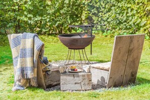 An outdoor cooking setup with a grill, a blanket, and a wooden table with food items. - 1 Bed in Trefeitha (oc-h32936) (Trefeitha)