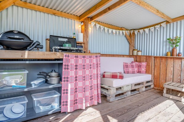A rustic cabin interior with a wooden bench, a grill, storage shelves, and a patterned curtain. - 1 Bed in Trefeitha (oc-h32936) (Trefeitha)