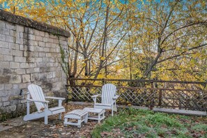 Une terrasse avec des fauteuils Adirondack et une petite table, entourée d’un mur de pierres et d’une clôture en bois.