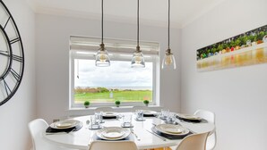 Comedor con un ventanal grande, mesa blanca y sillas.