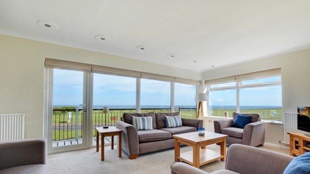 Amplia sala de estar con un gran ventanal que ofrece vistas al mar. Hay dos sofás, una mesa de centro y un mueble para la televisión.