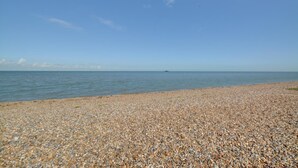 Ein Kiesstrand mit blauem Himmel und ruhiger See.