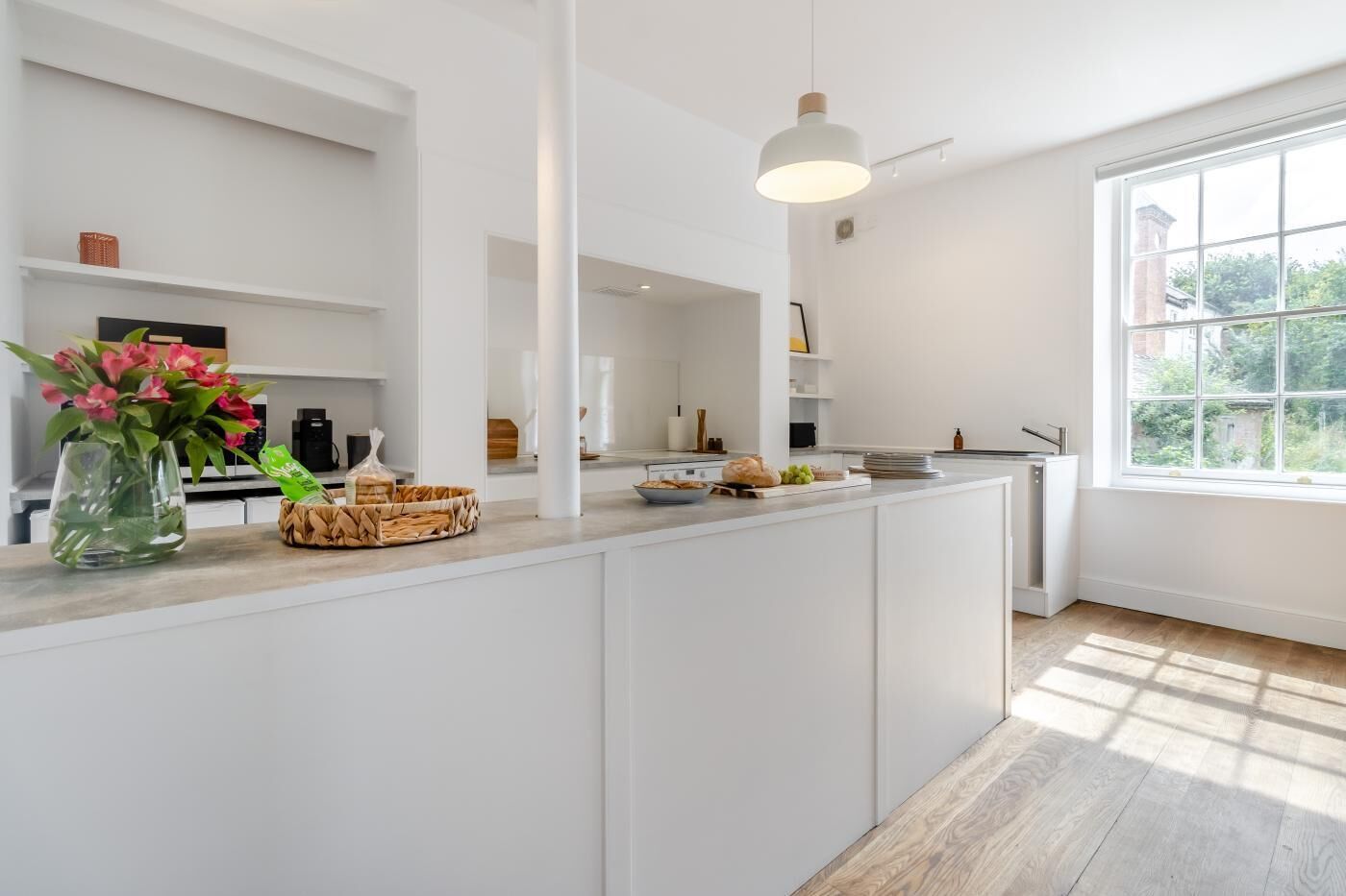 A modern kitchen with white cabinetry, a central island, and a large window providing natural light.