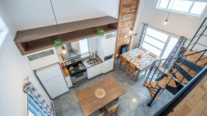 A modern kitchen with a central island, wooden ceiling beams, and a dining area with a staircase. - Chalet Chic et Spa | St-Come (Saint-Côme)