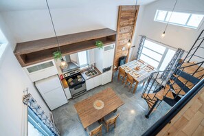 A modern kitchen with a central island, wooden ceiling beams, and a dining area with a staircase. - Chalet Chic et Spa | St-Come (Saint-Côme)
