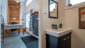 A compact kitchen with a wooden accent wall, a dining area with a plaid tablecloth, and a modern sink. - Chalet Chic et Spa | St-Come (Saint-Côme)