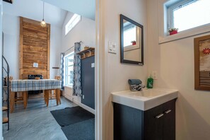 A compact kitchen with a wooden accent wall, a dining area with a plaid tablecloth, and a modern sink. - Chalet Chic et Spa | St-Come (Saint-Côme)