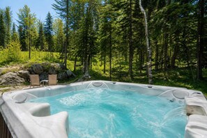 A hot tub surrounded by a forest with chairs and rocks. - Chalet Chic et Spa | St-Come (Saint-Côme)