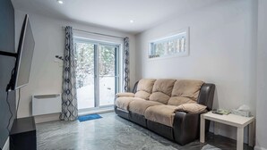 A modern living room with a sofa, a small table, a TV, and a large window. - Chalet Chic et Spa | St-Come (Saint-Côme)