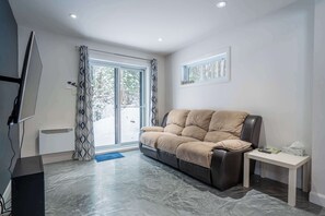 A modern living room with a sofa, a small table, a TV, and a large window. - Chalet Chic et Spa | St-Come (Saint-Côme)