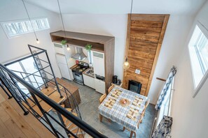 A kitchen with a stove, oven, and wooden wall. There is a table with a checkered tablecloth and a plant on the counter. - Chalet Chic et Spa | St-Come (Saint-Côme)