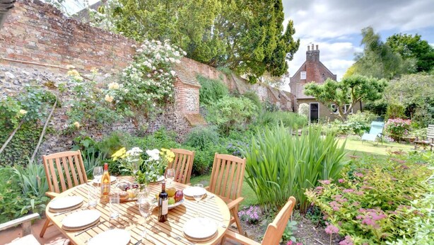Un jardín con una mesa lista para comer, rodeado de follaje y un muro de ladrillo.