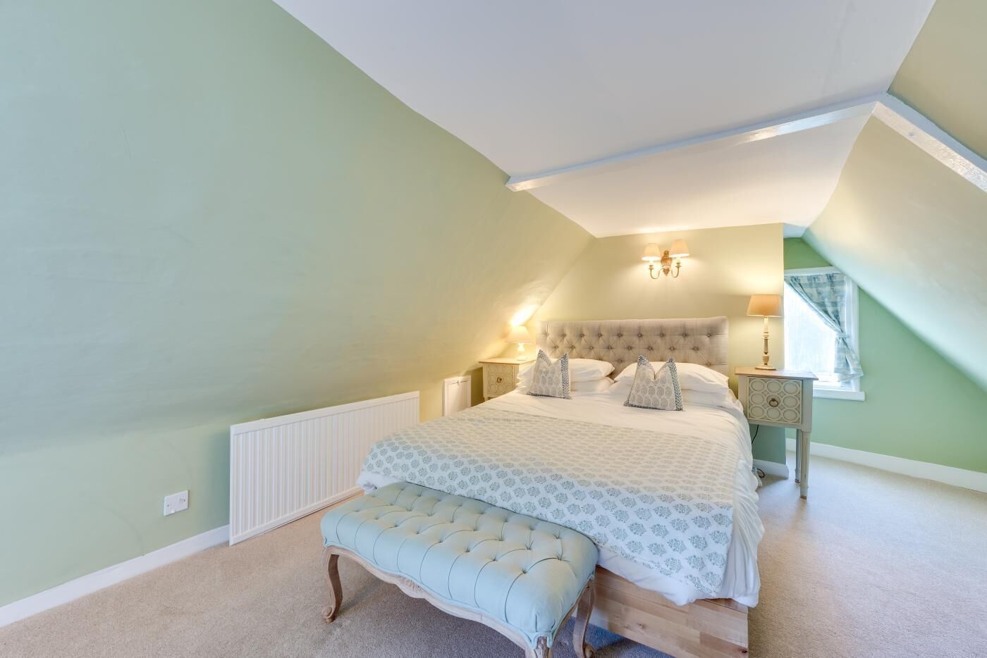 Une chambre à coucher avec un grand lit, un banc, une table de chevet et une lampe.