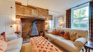 Una sala de estar con chimenea de ladrillo, un sofá, un reposapiés y una ventana con cortinas.