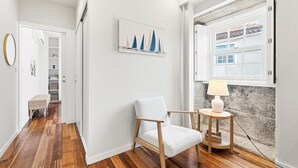A modern interior with a white chair, a small table with a lamp, and a view of the outside through a window. - GuestReady - Charming Porto Retreat Near the Sea (Porto)