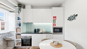 A modern kitchen with white cabinets, a microwave, and a sink. There is a dining table with chairs and a small plant on the window sill. - GuestReady - Charming Porto Retreat Near the Sea (Porto)
