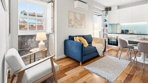 A modern living room with a blue sofa, a small table with a lamp, and a view of the outside through a window. - GuestReady - Charming Porto Retreat Near the Sea (Porto)